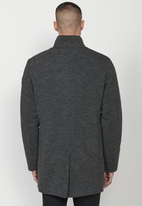 Abrigo de mezcla de lana gris con cuello alto, mangas largas, bolsillos laterales y corte recto, con una abertura en la parte posterior para facilitar el movimiento.