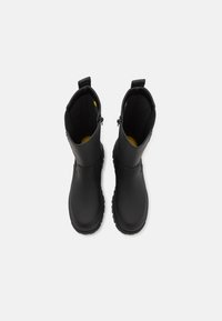 Bottes imperméables noires avec une tige haute, en matériau lisse semblable au caoutchouc, semelles texturées et semelles intérieures jaunes contrastantes. Dotées de languettes de traction en haut.