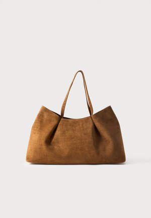 Sac cabas en cuir marron texturé avec deux fines anses, forme rectangulaire large et motif crocodile discret sur un fond uni clair.