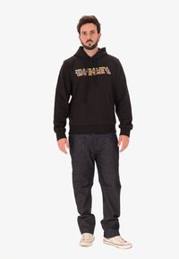 Felpa nera con logo "DIESEL" multicolore, dotata di tasca a marsupio e cappuccio con cordino. Abbinata a jeans scuri e sneakers.