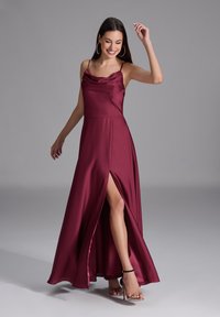 Robe maxi en satin bordeaux avec des bretelles spaghetti, un décolleté drapé et une fente haute jusqu'au haut de la cuisse. Elle présente une silhouette fluide et une texture lisse.