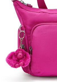 Pink nylon handbag with a textured finish. Features a front pocket and a furry pink monkey keychain attached to a silver clip.