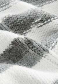 Siva i bijela pletena deka s teksturiranim uzorkom koji prikazuje izmjenične pruge, nudeći mekanu, dlakavu površinu.