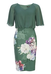 Blouse verte à manches courtes et fluides avec un décolleté en V profond, associée à une jupe crayon ajustée imprimée de fleurs avec des motifs clairs et foncés.