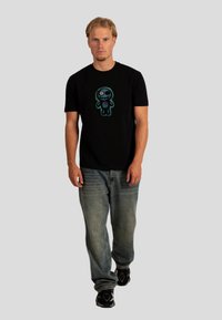 Czarna koszulka z krótkim rękawem z kolorową grafiką postaci z przodu, w zestawie z niebieskimi dżinsami i czarnymi trampkami.