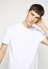 White cotton t-shirt with a crew neck, short sleeves, and rolled cuffs, featuring a relaxed fit and smooth texture.