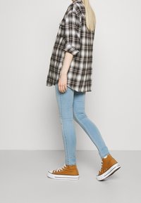 Camisa a cuadros en blanco y negro con mangas enrolladas, combinada con jeans skinny de color azul claro y zapatillas altas marrones con suelas blancas.