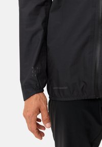 Giacca da ciclismo nera con una texture morbida, dotata di polsini elastici e di un logo visibile. Leggera, progettata per comfort e durata.