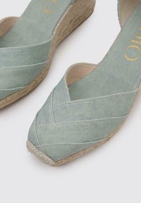Zapatos de cuña de lona verde menta con diseño entrelazado, suela envuelta en yute natural y punta redonda. Textura suave y tacón bajo para mayor comodidad.