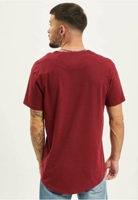 Mørkerød bomuld t-shirt med buet kant, korte ærmer og en afslappet pasform, set bagfra med synlige syninger.