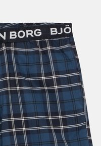 Tissu à carreaux bleu et noir avec des lignes blanches, ceinture élastique montrant partiellement le nom de marque "BJÖRN BORG" en lettres blanches.