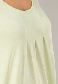 Top verde chiaro con scollatura a girocollo, caratterizzato da pieghe verticali vicino al centro per aggiungere texture e volume. Tessuto morbido con una finitura liscia.