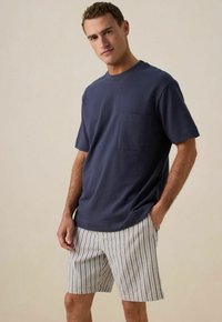 T-shirt bleu marine à manches courtes avec une poche poitrine, associé à un short clair à rayures verticales bleu et crème. Style décontracté, coupe relax.
