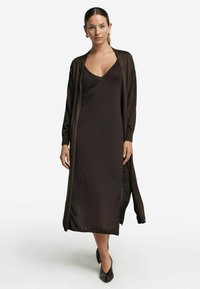 Lång mörkbrun klänning med V-ringning, tillsammans med en matchande öppen cardigan. Tyget verkar mjukt med en slät textur.