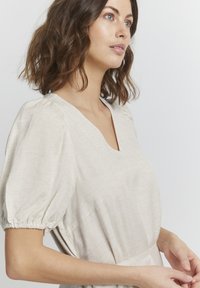 Bežs lina kleita ar V veida kaklu un puff piedurknēm. Mīksts audums, pieguļošs jostas vieta un smalki dūrieni. Vienkāršs un elegants dizains.