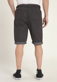 Dunkelgraue Jeansshorts mit umgeschlagenen Säumen, ausgestattet mit zwei Gesäßtaschen und dezenten Nähten. Getragen mit schwarzen High-Top-Sneakern.