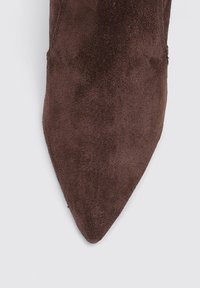 Chaussure en suede brun à bout pointu avec une texture lisse, affichant un ajustement étroit et sans matériel ou accents visibles.