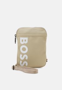 Borsa a tracolla in nylon beige con chiusura a zip, grande logo bianco "BOSS", superficie testurizzata e tracolla regolabile a righe.