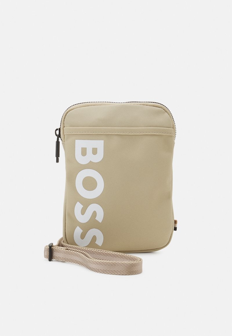 Beige nylon olkalaukku, jossa on vetoketjukiinnitys, suuri valkoinen "BOSS"-logo, teksturoitu pinta ja raidallinen säädettävä hihna.