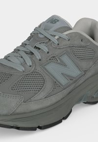 Γκρι αθλητικό παπούτσι New Balance με πάνελ από σουέτ και δίχτυ, γκρι κορδόνια, λογότυπο στο πλάι και επενδεδυμένη σόλα σχεδιασμένη για άνεση και στήριξη.
