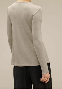 Långärmad, ljusgrå topp i strukturerad tyg med en subtil glans. Har rund halsringning och vågiga manschetter.