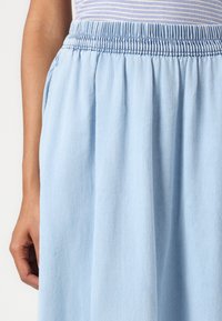 Gonna leggera di colore azzurro chiaro con una vita elasticizzata e tessuto fluido. La texture è liscia con una leggera lucentezza. Nessun motivo visibile.