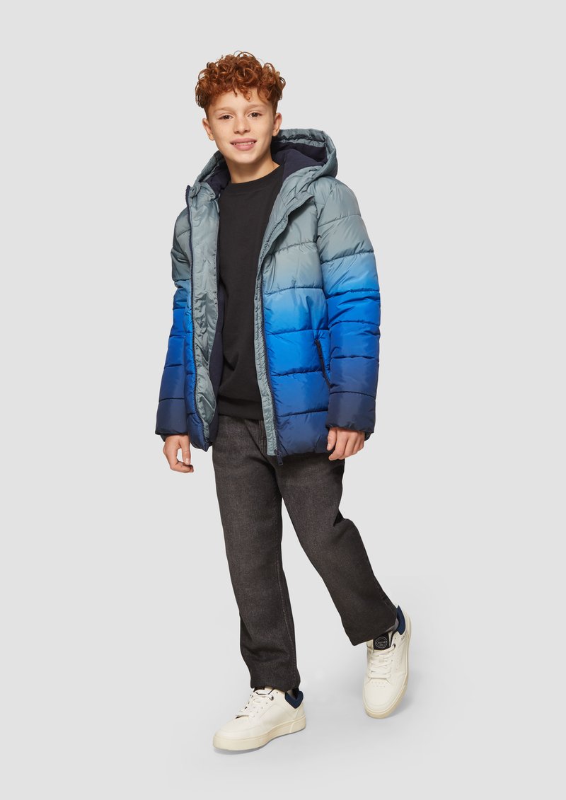 Giubbotto imbottito in gradiente di blu e grigio. Dotato di cappuccio, chiusura con cerniera e texture trapuntata. Abbinato a pantaloni scuri e sneakers bianche.