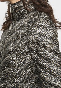 Veste rembourrée imprimée léopard avec un schéma de couleurs or et noir. Dotée d'un col haut et de zippers, avec un accent de logo circulaire sur la manche.