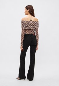 Haut à carreaux décolleté épaules dans des tons marron doux, avec tissu froncé. Associé à un pantalon noir évasé et des sandales à talons.