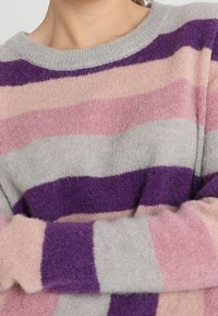 Sweter dzianinowy w paski w kolorze szarym, różowym i fioletowym. O okrągłym dekolcie i długich rękawach, wykonany z miękkiego teksturowanego materiału.