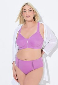 Paarse bh en high-waisted slip set, gemaakt van gladde stof met glanzende accenten. Model draagt een wit shirt. Eenvoudige, moderne snit, geen patronen.