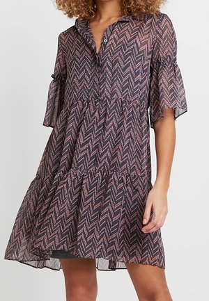 Woman wearing a knee-length, long-sleeve dress with a pink and black zigzag pattern and a tiered skirt.