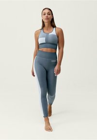 Sportovní dvoudílný outfit obsahující šedý crop top s bílými akcenty a odpovídající legíny, zdůrazňující pružný design a měkkou texturu.