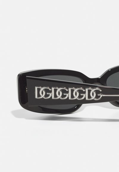 Black sunglasses with a rectangular frame, featuring a glossy finish and a silver logo detail along the side. Dark lenses included.
