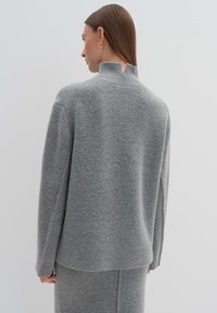 Grau gestrickter Pullover mit hohem Kragen, lockerer Passform und langen Ärmeln. Weiche Textur mit seitlichen Schlitzdetails und einer subtilen Naht.