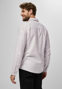 Ljuslila långärmad skjorta i tyg med en mjuk textur. Har knäppningar vid ärmsluten, en spetsig krage och en rundad nederkant.