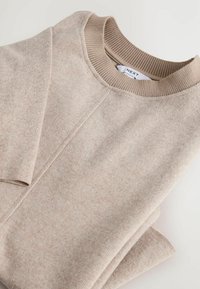 Maglione beige lavorato a maglia con collo e polsini a coste. Texture morbida e motivo sottile visibile, piegato ordinatamente, etichetta visibile all'interno del colletto.