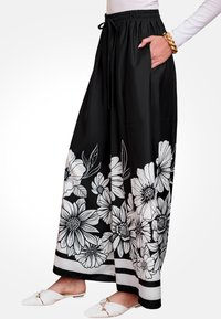Pantalones de pierna ancha negros con un estampado floral en blanco en el dobladillo, con cintura elástica y bolsillos laterales. Textura suave, tela ligera.