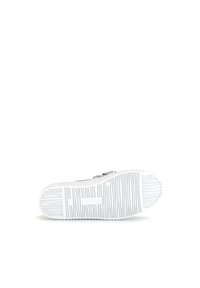 Baskets blanches plates avec une semelle en caoutchouc texturé, dotées d'un upper en tissu gris et d'une sangle ajustable pour un maintien sécurisé.