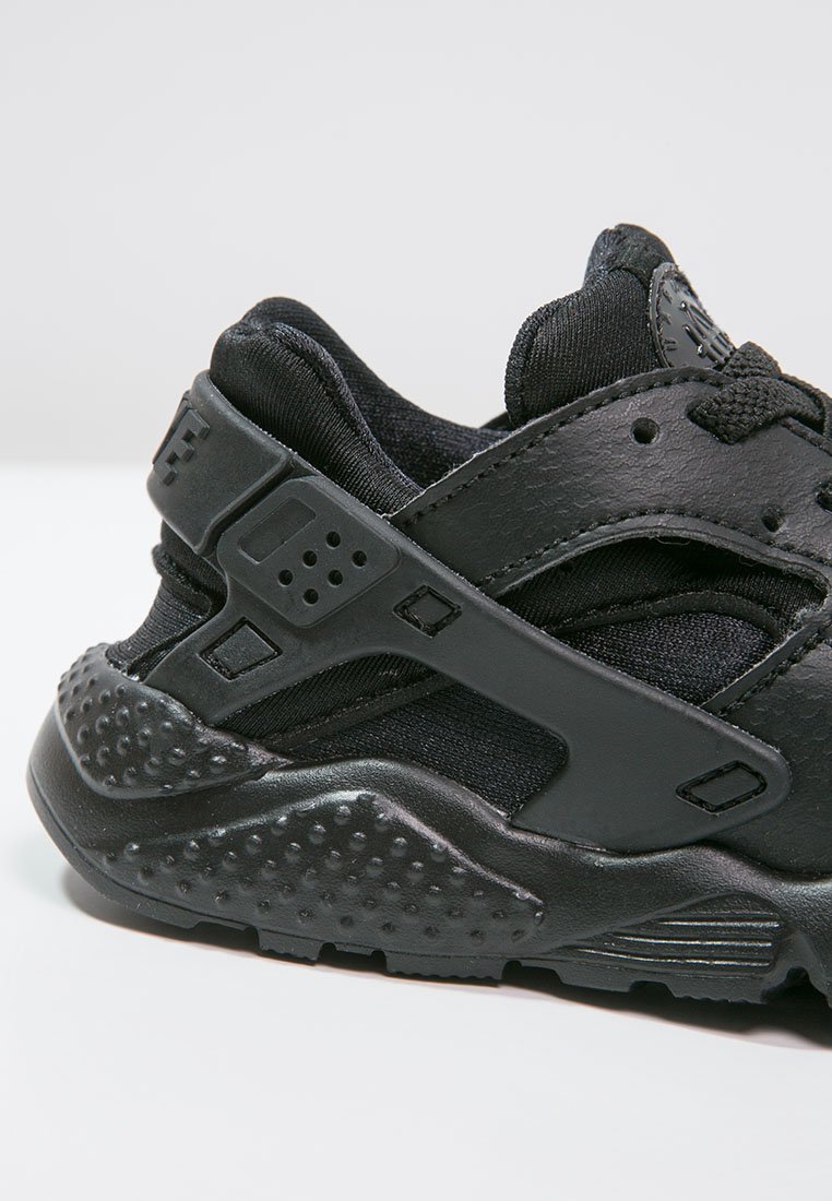 Zapatilla deportiva negra que combina materiales texturizados y lisos, con una suela de goma pronunciada y detalles de malla para mayor transpirabilidad.