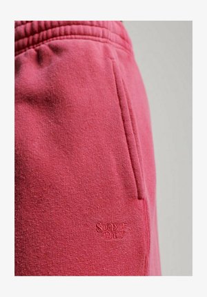 Pink sweatpants made of soft fleece with a textured finish, featuring an embroidered "Superdry" logo and side pocket detailing.