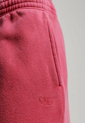 Różowe spodnie dresowe z miękkiego materiału, z prążkowanym pasem, boczną kieszenią i wypukłym logo "Super Dry" na nogawce. Teksturowany, casualowy design.