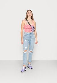 Top tank texturado rosa, jeans rasgados de cintura alta em azul claro, e sapatilhas roxas desportivas. Pequena bolsa crossbody roxa com padrão e alça preta.
