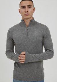 Maglione grigio con zip realizzato in tessuto lavorato a maglia, con colletto alto, polsini a coste e un dettaglio logo di lato. Texture delicata su tutto il materiale.
