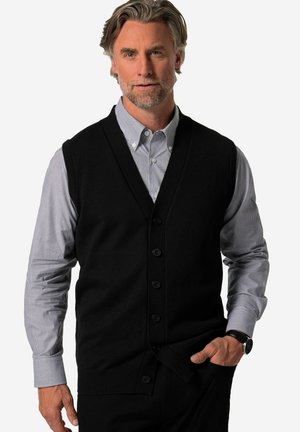 Gilet nero in maglia con scollo a V, bottoni frontali e una texture liscia, indossato sopra una camicia a righe leggera blu e bianca.