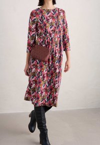 Kwiatowa sukienka w kolorze różowym, granatowym i zielonym, z rękawami 3/4 i rozkloszowanym dołem; zestawiona z brązową torebką na ramię o fakturze.