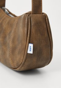 Sac en bandoulière en simili cuir marron avec une forme arrondie, des coutures visibles et une étiquette de marque. Surface texturée avec une finition lisse.