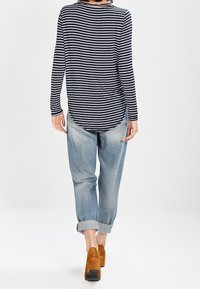 Maglietta a maniche lunghe a righe blu navy e bianche con fondo arrotondato, abbinata a jeans azzurri arrotolati e stivaletti con tacco marroni.