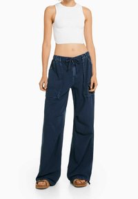 Granatowe spodnie o szerokich nogawkach z elastycznym paskiem, bocznymi kieszeniami i teksturowaną bawełnianą tkaniną. Noszone z dopasowanym białym topem typu crop.