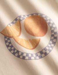 Καμβάς από βαμβάκι με σχέδιο που περιλαμβάνει μια φέτα εσπεριδοειδούς σε πορτοκαλί και κίτρινο-πορτοκαλί χρώμα πάνω σε μπλε καρό δαχτυλίδι, με φόντο σε ανοιχτό χρώμα.